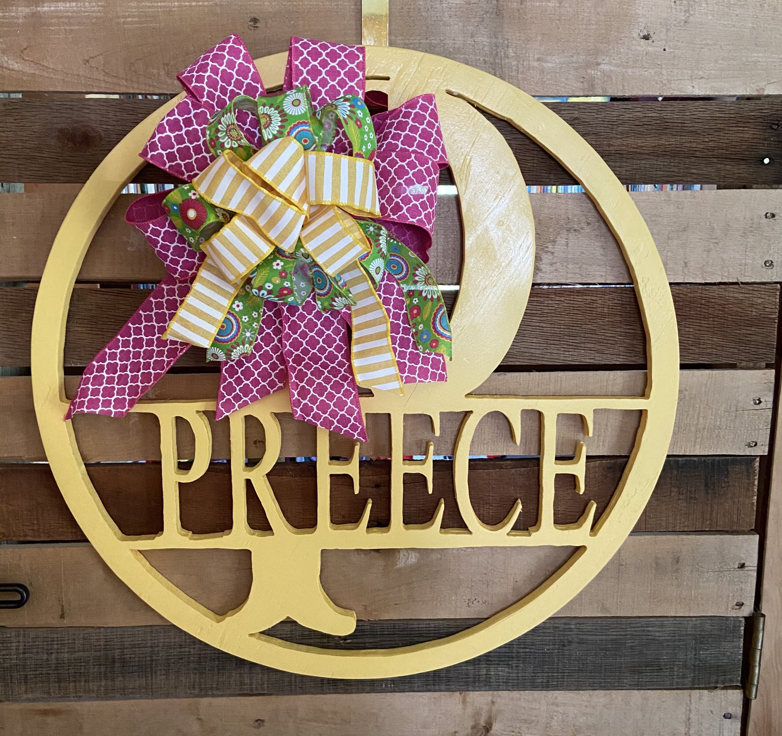 Round yellow, with the initial P and name Preece routed out of the center with a pink, green, and yellow bow attached to the sign.