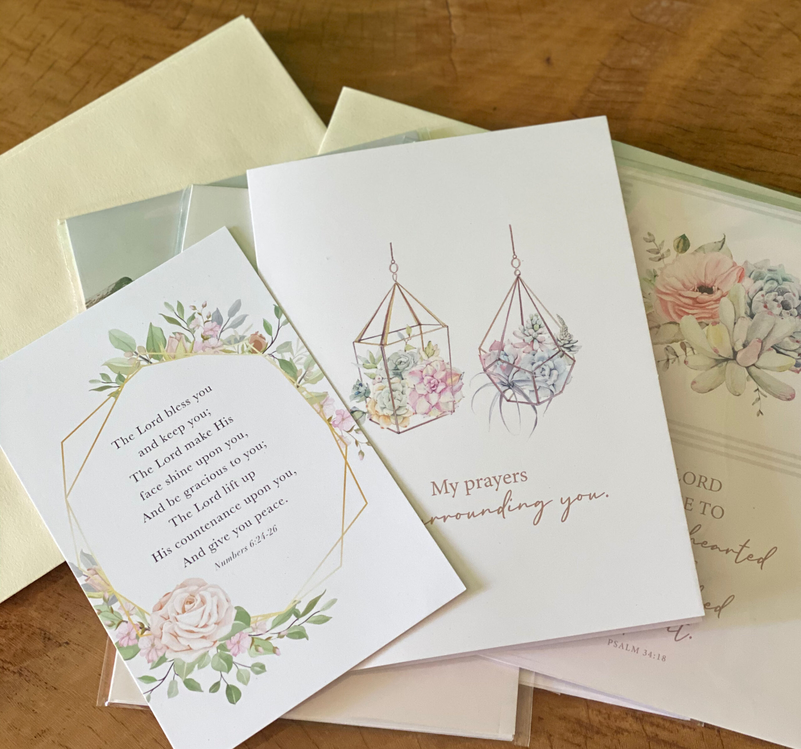 Assortment of white christian note cards with pink and blue flowers lying flat on a table.