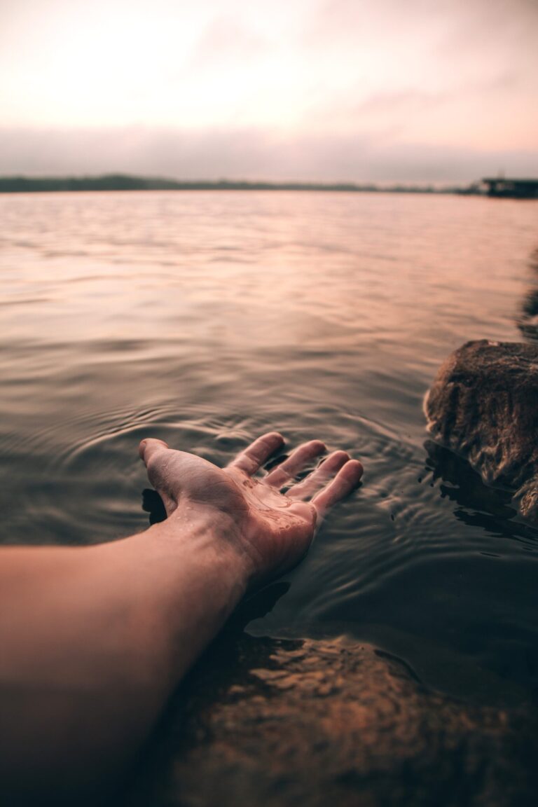 A hand resting on a body of water from Pexels.