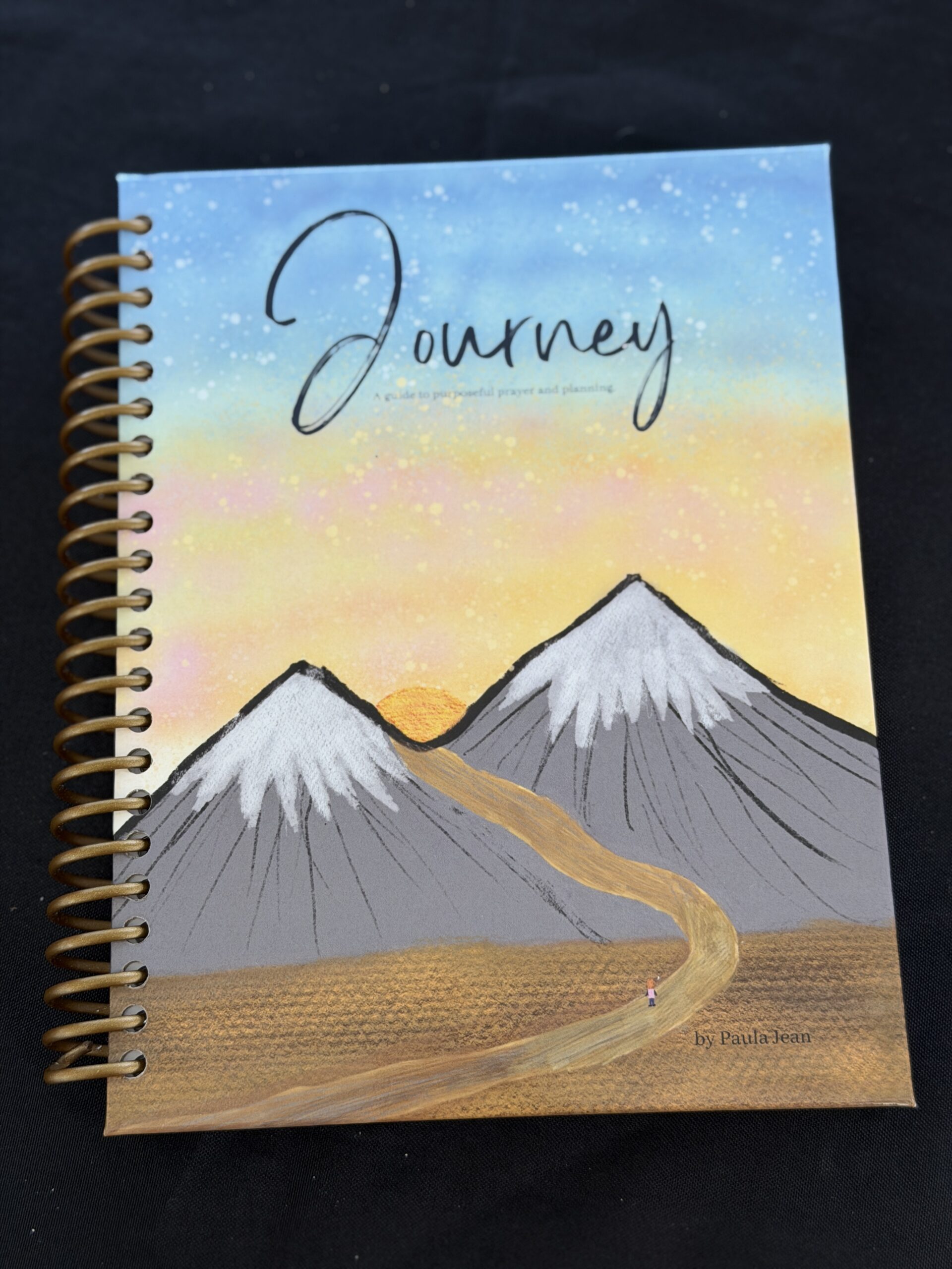 Planner with the blue sky, warm yellow sun, snow capped mountains, and a girl on a girl with a pink backpack walking on a road.