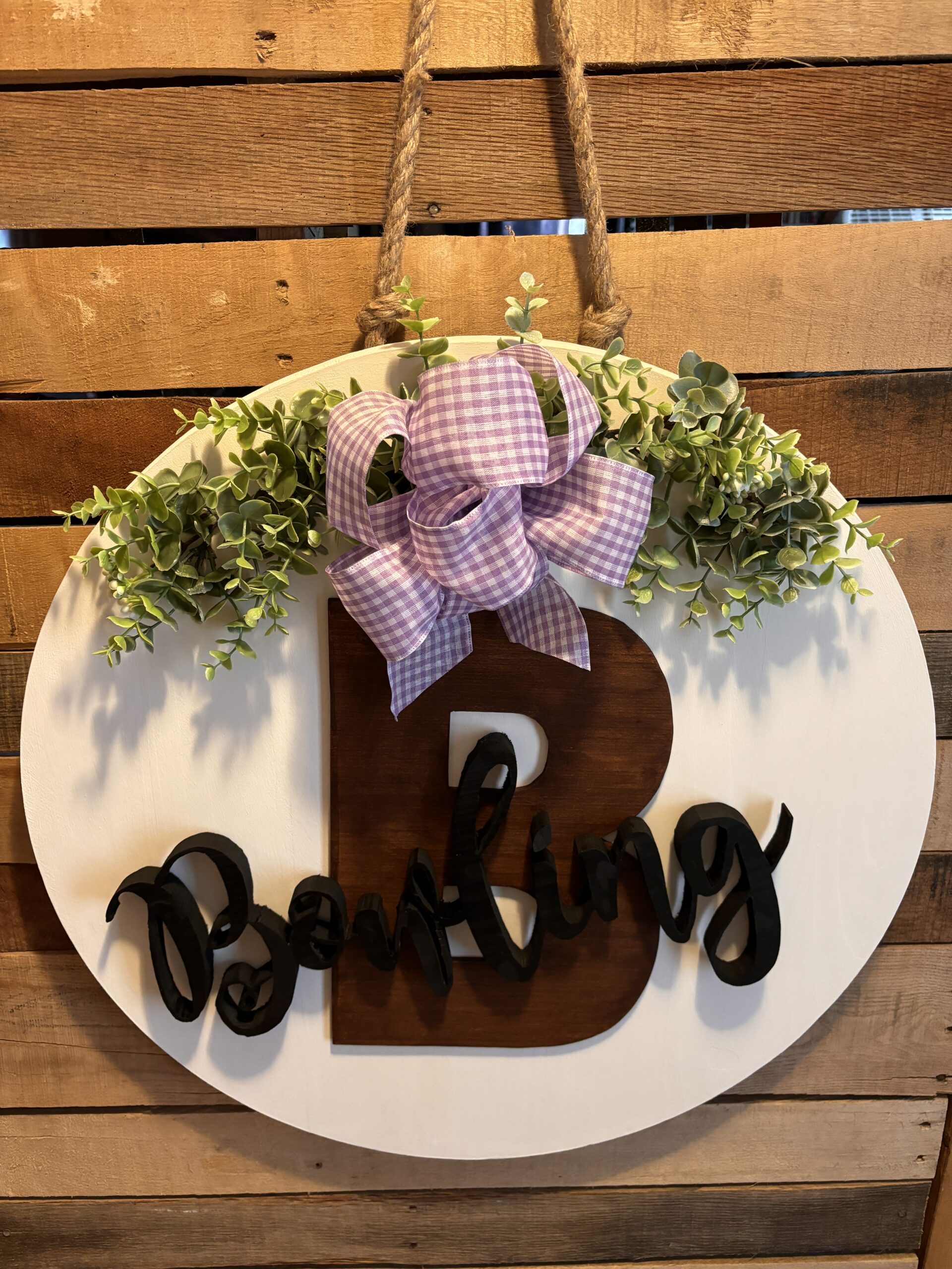 Round white door hanger sign with a 3-D Letter B in brown and a 3-D name Bowling in black. Also pictured is a light purple bow and greenery.